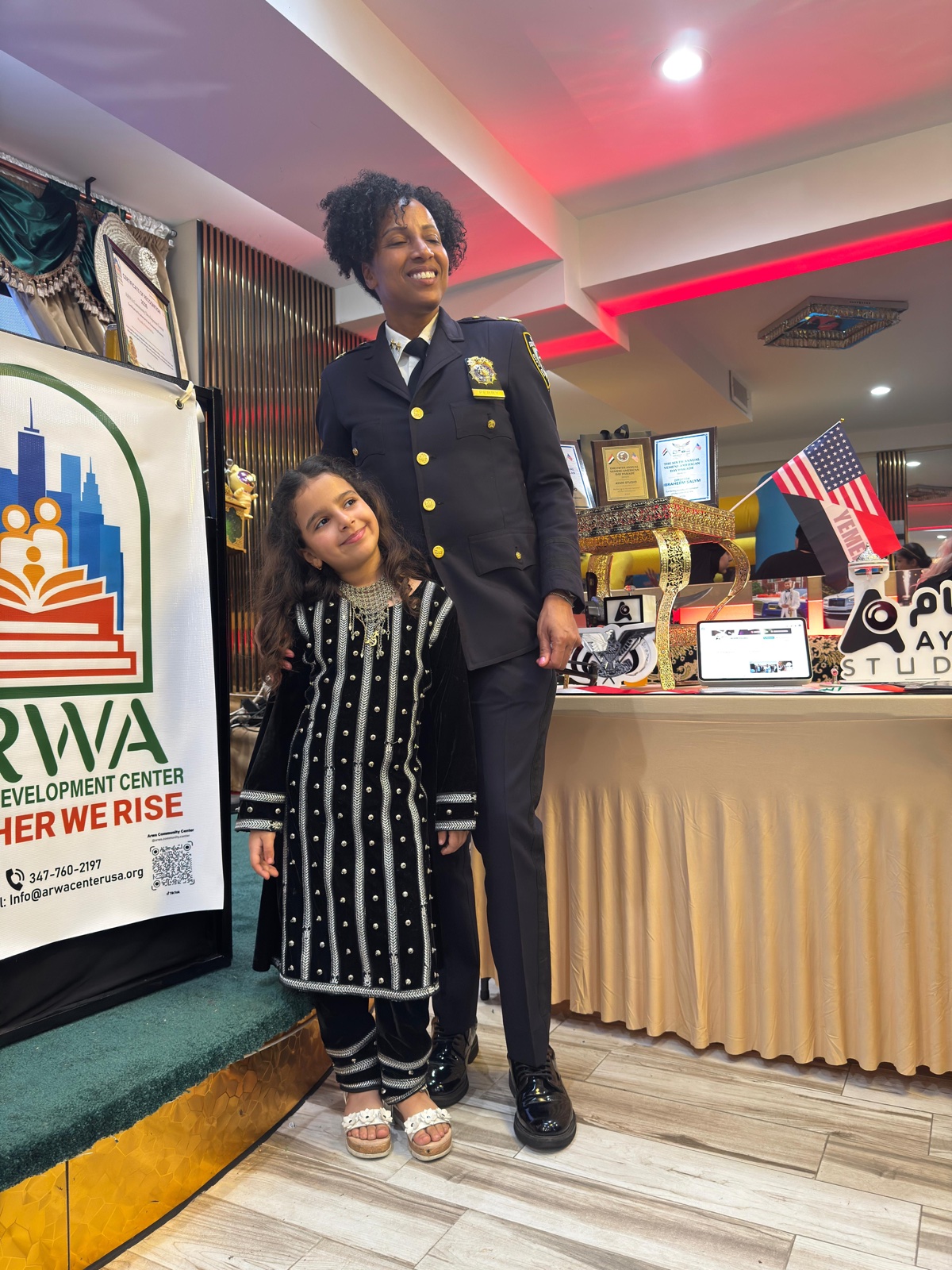 NYPD officer with a young community member at an ARWA community recognition event, with Yemeni and American flags